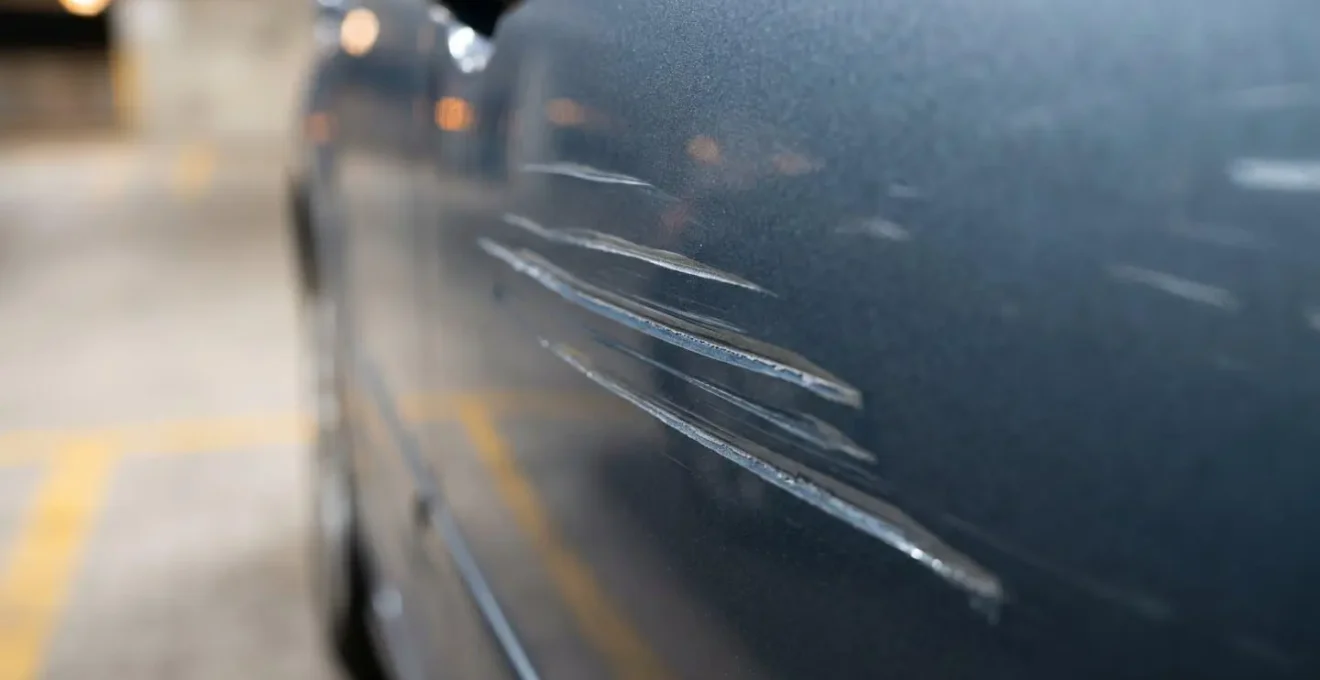Gros plan sur une carrosserie de voiture endommagée par un acte de vandalisme avec rayures profondes, illustrant la nécessité de prouver l'acte malveillant