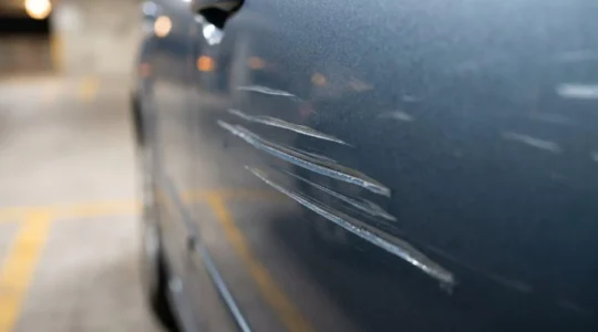 Gros plan sur une carrosserie de voiture endommagée par un acte de vandalisme avec rayures profondes, illustrant la nécessité de prouver l'acte malveillant